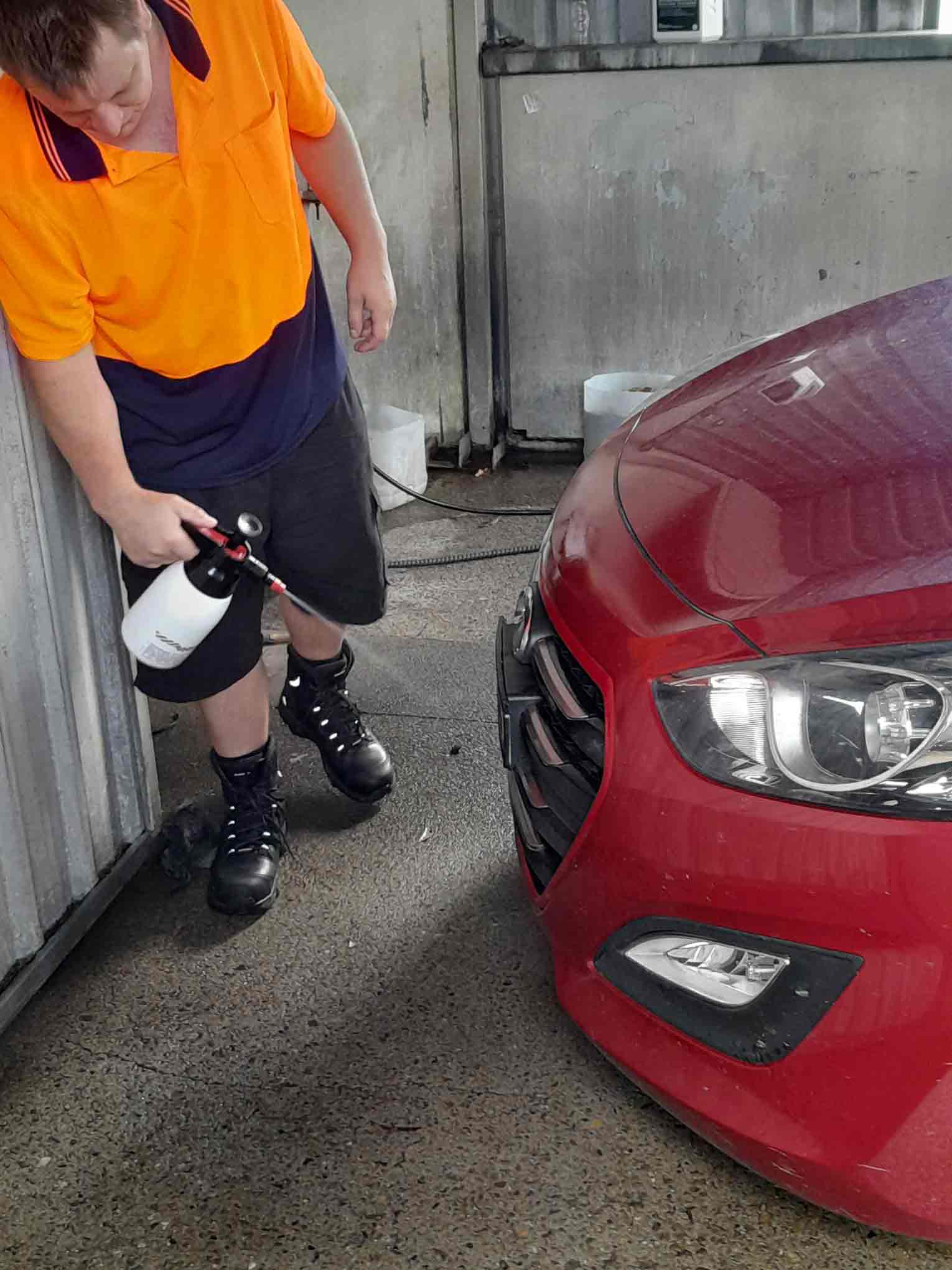 Man in orange high-vis washing down front of a red car. 