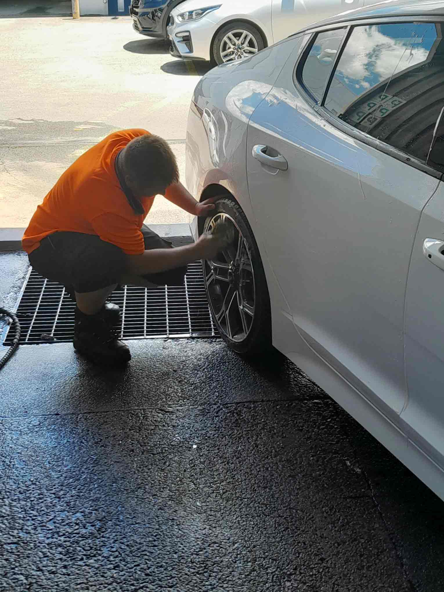 Man in orange high-vis washing wheel rims on car. 