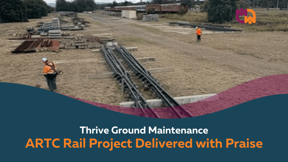 Two Thrive Ground Maintenance workers in high visibility gear work across a large open rail storage yard in Denman, with rail sleepers, steel structures, and tracks visible across the site. Text overlay reads "Thrive Ground Maintenance: ARTC Rail Project Delivered with Praise."